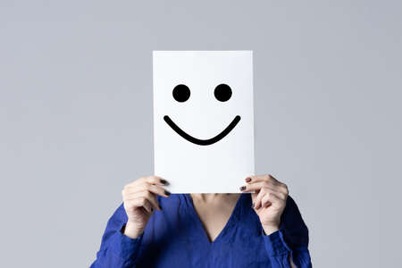 The girl holds a white sheet with a smile in front of her face.の写真素材