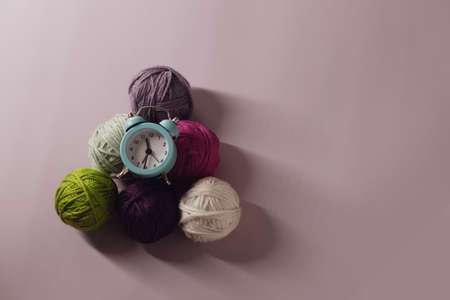 A small green alarm clock lies on woolen balls against a lilac background. Time to knitの写真素材