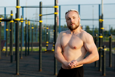 In the morning at sunrise, a man with an interesting braid hairstyle poses like a bodybuilder with a...