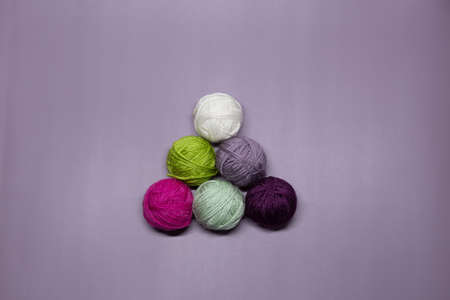 Balls of multi-colored woolen threads for knitting in the form of a pyramid lie on a purple background.の写真素材