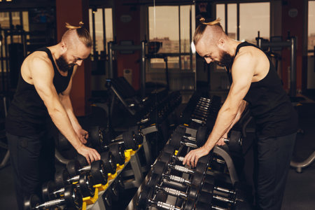 A man lifts heavy dumbbells in a fitness clubの写真素材