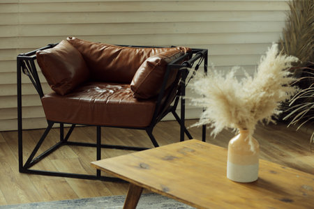 A brown leather armchair in a room with a table and a vase of dry grass.の写真素材