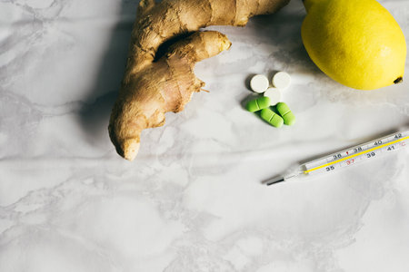 A set from a cold or flu - ginger, lemon, pills and a thermometer are on a white tableの写真素材