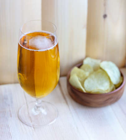 Close up of a glass of blonde beer with a cup of chips on the wooden background. Good for beer festival, pub, restaurant advertising.の写真素材