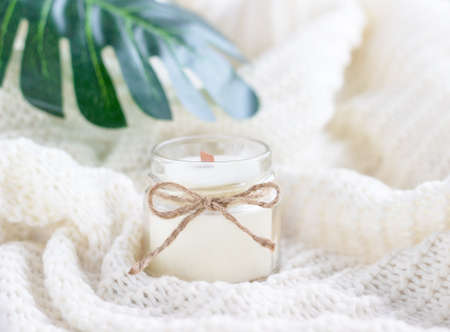 White wax candle in glass with green leaves on the blurred background