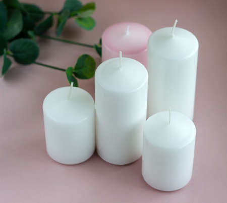 Set of white and pink wax candles with green leaves on the pink backgroundの写真素材
