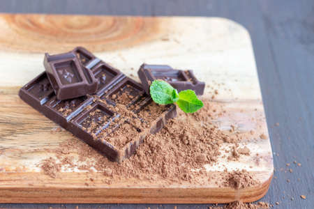 Dark chocolate bar on the wooden board with mint leaves. Tasty, delicious chocolate.
