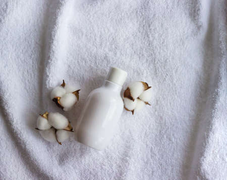 White plastic bottle for cosmetics with cotton flowers on the white towel. Spa wellness concept.
