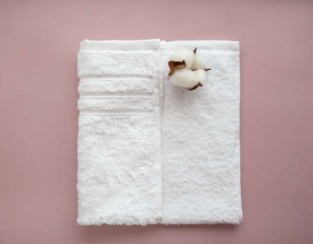 Folded white cotton towel with cotton flower on the light background. Center composition. SPA...