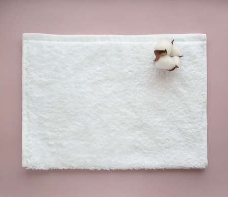 Folded white cotton towel with a flower of cotton on the light background. top view. SPA concept.の写真素材