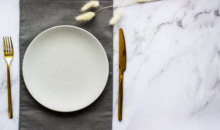 Elegant table setting with empty gray plate, golden cutlery on linen napkin. table decor. copyspace.