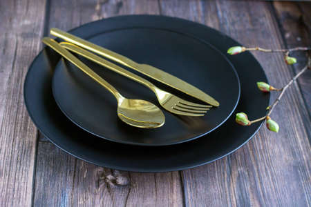 Close-up of table setting with black plate, gold cutlery with tree branch on the wooden table. Dining setting. high quality photoの写真素材