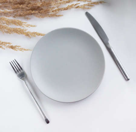 Gray empty plate with silver cutlery on the white table decorated by dried flowers. Dining table decor.の写真素材