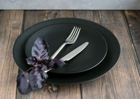 Table setting with black plate, silver cutlery with basil leaves on the wooden table. high quality photoの写真素材