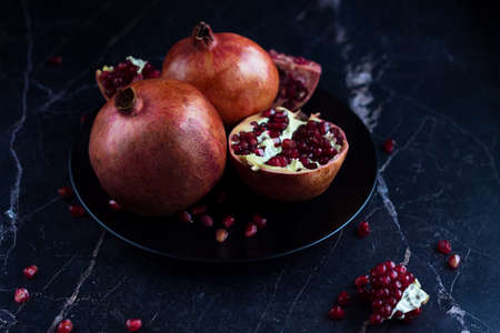 Pomegranate fruits on the black plate on the marble table.
