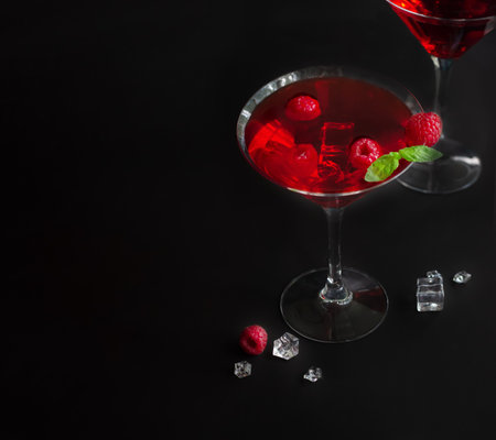 Red alcohol raspberry cocktails in martini glass with mint on the black background. Copy space. Selective focus.の写真素材
