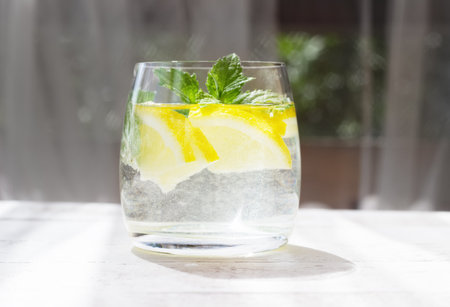 Close-up of homemade lemonade with lemon, mint and ice cubes in a glass on white wood tableの写真素材