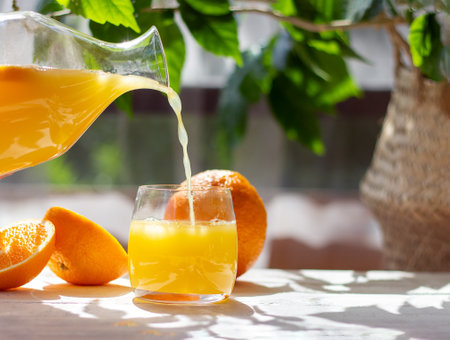 Orange juice pouring from pitcher into glass. Healthy citrus drink. Summer freshness concept.の写真素材