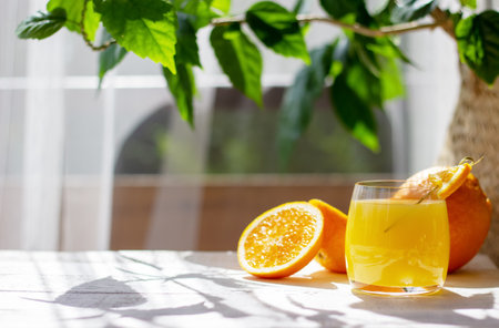 Glass of fresh orange juice with ripe oranges on the white wooden table in the summer terraceの写真素材