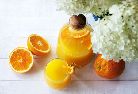 Top view of fresh orange juice in pitcher and glass with ripe oranges on the white wooden table in...