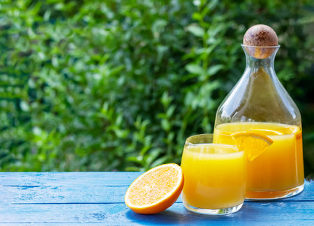 Fresh orange juice in pitcher and glass with ripe oranges on the blue wooden tableの写真素材