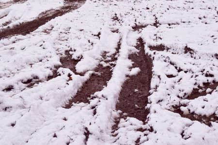 Dirty road with tire prints on wet soil and melted snow, outdoor background.の写真素材