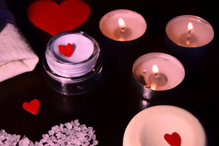 Valentine's day Spa style. a dark table on which one big red heart and small hearts on soap with lighted candles and cream with a place for writing in pink. selective focusの写真素材