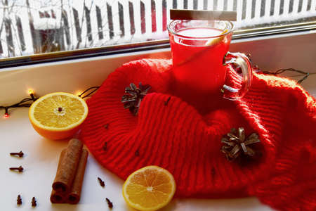 Mulled wine with spices and a red scarf on a light windowsill. Christmas holiday and home warmth...