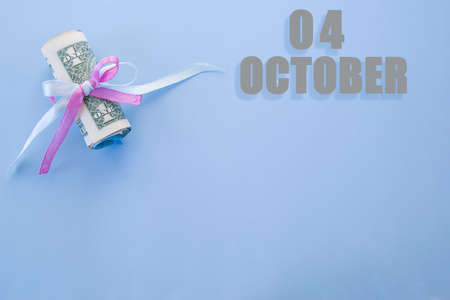 calendar date on blue background with rolled up dollar bills pinned by blue and pink ribbon with copy space. October 4 is the fourth day of the month.の写真素材