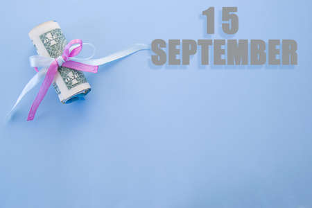 calendar date on blue background with rolled up dollar bills pinned by blue and pink ribbon with copy space. September 15 is the fifteenth day of the month.の写真素材
