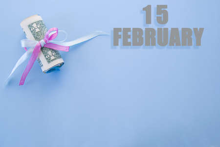 calendar date on blue background with rolled up dollar bills pinned by blue and pink ribbon with copy space. February 15 is the fifteenth day of the month.の写真素材