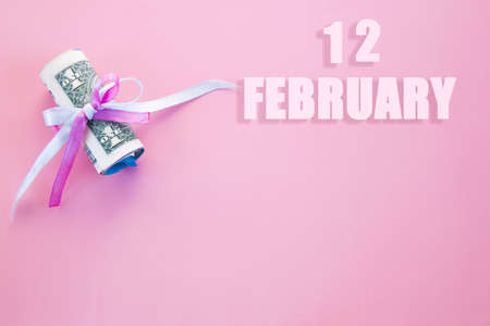 calendar date on pink background with rolled up dollar bills pinned by pink and blue ribbon with copy space. February 12 is the twelfth day of the month.の写真素材