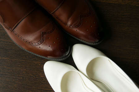 Brown mens shoes and white womens shoes on a dark wooden background, top viewの写真素材