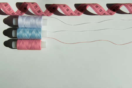 Three spools of thread and a yellow centimeter ribbon on a light background. Needlework and sewing...