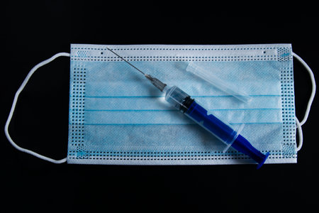 Disease. Medical mask and syringe on a dark background. Solid dark background with medical instruments.の写真素材