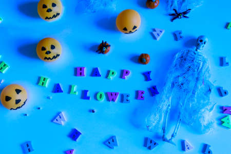 Halloween concept with pumpkins, skeleton, toy spiders and happy halloween lettering on blue backgroundの写真素材