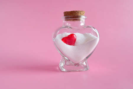 Red heart shape on white salt in a heart shaped glass jar. the concept of the holiday of all lovers on February 14.の写真素材