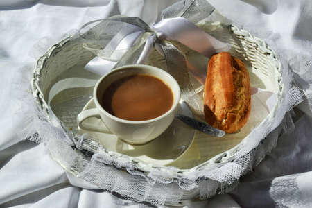 Breakfast in bed in a hotel room. Morning coffee with cream and eclair on white bed linen.