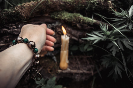 burning candles and a womans hand with a bracelet on a dark natural background. pagan wiccan, slavic traditions. Witchcraft, esoteric spiritual ritual for mabon, halloween, samhain. autumn equinox festival.の写真素材