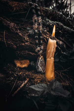 burning candle, a symbol of the moon, an amulet lying on the moss on a dark natural background. pagan wiccan, slavic traditions. Witchcraft, esoteric spiritual ritual for mabon, halloween, samhain. autumn equinox festival.の写真素材