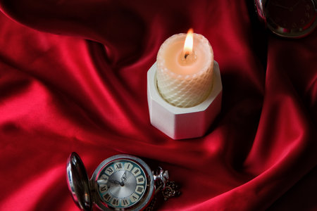 White burning candle on a red background with an old pocket watch, postcard on a blue background. Table decor for a festive dinner, Witchcraft, esoteric spiritual ritual. autumn equinox festival.の写真素材