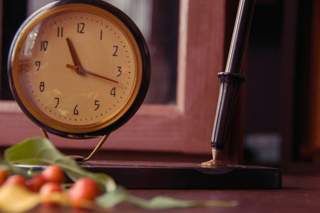 Vintage desk clock with ink fountain pen and apple tree leaves with small apples on wooden background with bokeh. Autumn season picture style.の写真素材