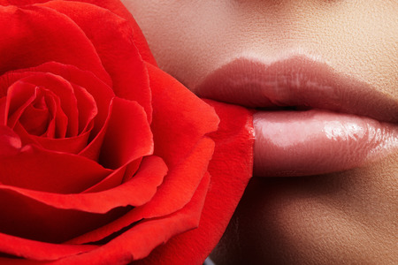Close-up beautiful female lips with bright lipgloss makeup. Perfect clean skin, light fresh lip make-up. Beautiful spa portrait with tender pink rose flower. Spa and cosmeticsの写真素材