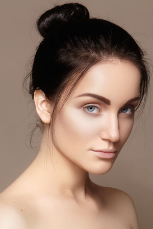 Beautiful young woman with clean face, shiny skin, fashion natural make-up, perfection eyebrows. Cute bun hairstyle. Spa portrait, naturel cosmetics, healthy fresh lookの写真素材
