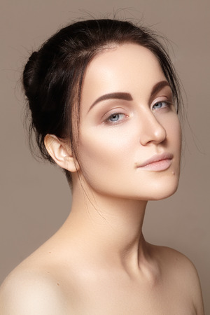 Beautiful young woman with clean face, shiny skin, fashion natural make-up, perfection eyebrows. Cute bun hairstyle. Spa portrait, naturel cosmetics, healthy fresh lookの写真素材