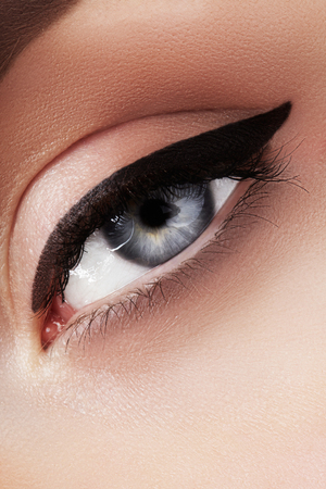 Close-up macro of beautiful female eye with perfect shape eyebrows. Clean skin, fashion naturel make-up. Good vision. Classic fashion eye liner makeup. Black eyeliner and brown eyeshadowsの写真素材