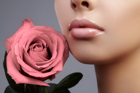 Close-up beautiful female lips with bright lipgloss makeup. Perfect clean skin, light fresh lip make-up. Beautiful spa portrait with tender pink rose flower. Spa and cosmeticsの写真素材