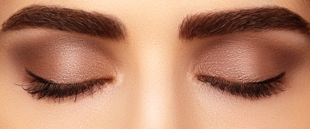 Beautiful macro shot of female eye with classic smoky makeup. Perfect shape of eyebrows, brown eyeshadows and long eyelashes.Closeup macro shot of fashion smoky eyes visage. Before and afterの写真素材