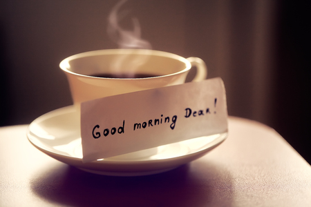 White ceramic cup of tea or coffee with nice letter 'good morning dear' on kitchen wood table. Beautiful photo with breakfast.の写真素材