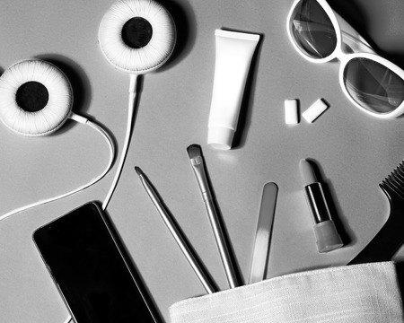 Above view of woman bag stuff . Set of female cosmetics and accessories. Glamour tools and beauty objects. Black and white photo of headphones, sunglasses and smartphoneの写真素材